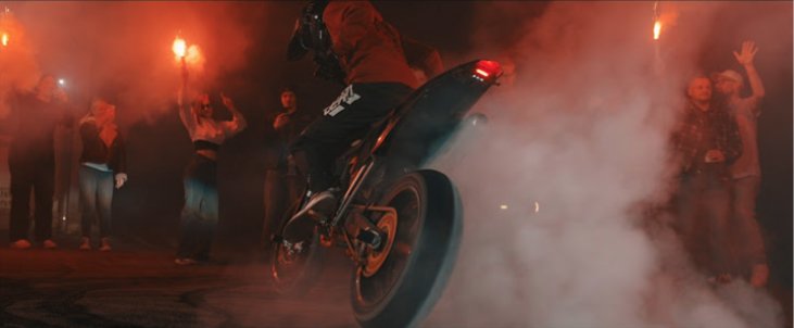 Szene aus dem Musikvideo: ein Motorrad macht einen Burnout, um es herum Leute mit Bengalos im Rauch